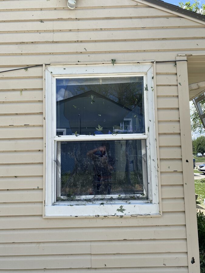 Hail damage to vinyl siding and window frame on Omaha home